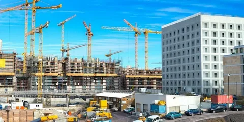 Two large commercial construction sites with multiple tower cranes building complex structures against a blue sky.