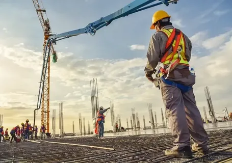 Construction worker on a site with rebar and concrete pump, representing detailed material and quantity takeoff services.