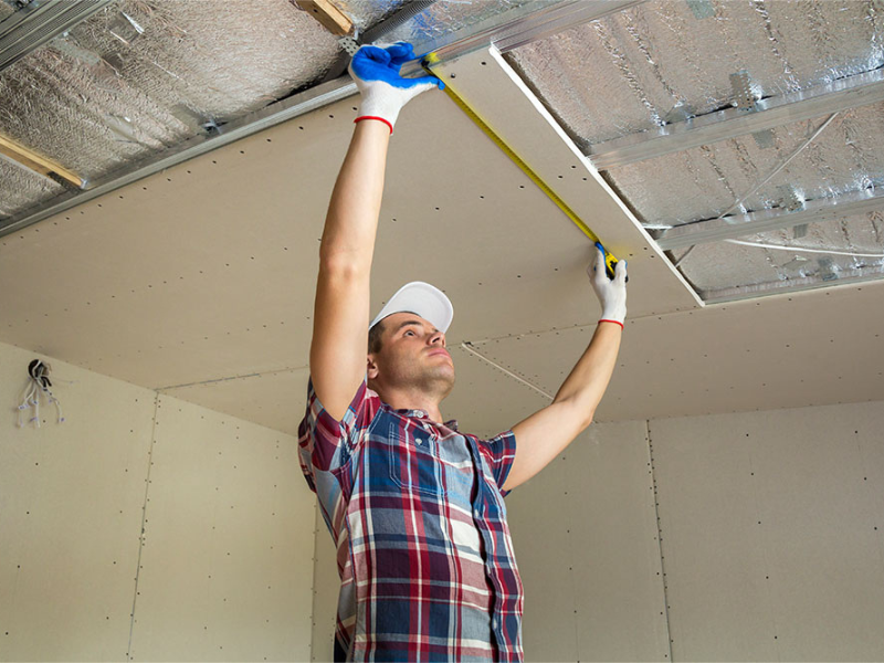 Worker measuring ceiling for drywall installation, representing ALM Estimating’s drywall estimating services