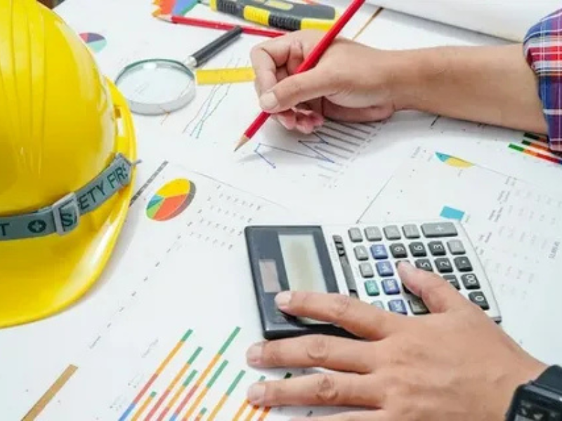 Construction cost estimating services showing a professional calculating project costs with drawings, charts, and safety helmet by ALM Estimating