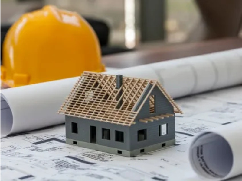 House model on blueprints with hard hat, representing ALM Estimating’s residential estimating services